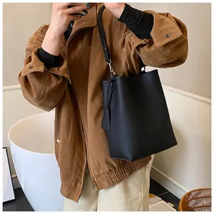 Gros plan d'un sac seau noir en cuir grainé avec bandoulière porté par un mannequin
