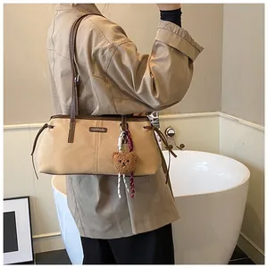 Detail of beige suede tote bag featuring brown leather straps and a cute plush bear charm