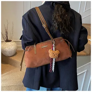 Detail of vintage brown suede tote bag with metal tag and plush bear charm on shoulder