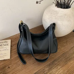 Sac hobo minimaliste en cuir noir avec surpiqûres blanches sur une table en bois