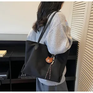 Schulteransicht einer schwarzen Shopper-Tasche mit süßem Bärenanhänger am Gurt