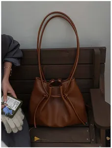 Detail of dark brown drawstring bucket bag on a wooden bench in autumn sunlight