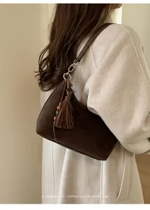 Chic dark brown suede shoulder bag with tassel detail shown on beige coat model