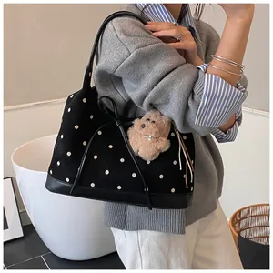 Detail of black polka dot canvas tote bag with leather straps and plush bear charm