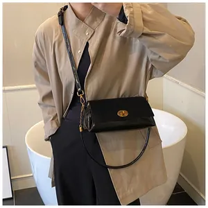 Détail d'un sac en cuir verni noir avec fermoir ovale doré et bandoulière réglable pratique