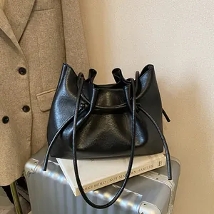 Minimalist black faux leather drawstring tote bag with slim straps on a silver suitcase