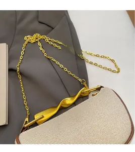 Close-up of beige fabric dumpling bag with gold metal twist bar and chain strap