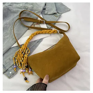 Detail of mustard yellow suede handbag with woven handle and colorful beaded tassel