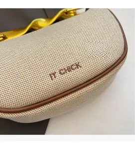 Detail of beige canvas saddle bag with brown leather trim and wavy gold metal buckle