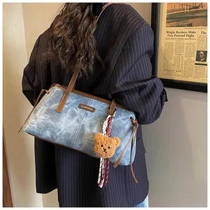 Detail of blue denim shoulder bag with brown strap and plush bear charm on model