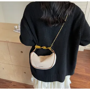 Detail of crescent moon bag featuring beige canvas, brown leather trim and gold metal handle