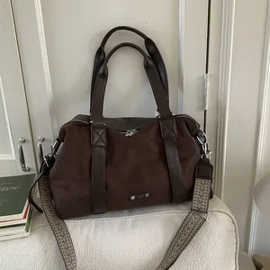 Minimalist large brown suede tote bag with geometric woven strap on a white sofa
