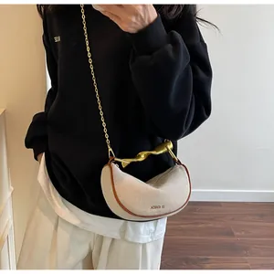 Detail of canvas dumpling bag with gold wavy handle and chain strap worn by a model