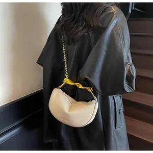 Close-up of beige crescent bag with gold chain strap on model in black leather jacket