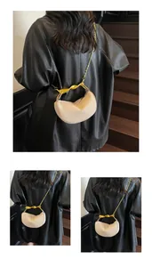 Detail of beige crescent bag featuring a golden twisted metal handle and fine chain strap