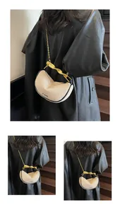 Detail of beige crescent bag with gold twisted handle and chain strap on a model