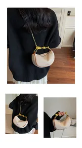 Detail of beige half-moon bag featuring a gold twisted handle and metal chain strap