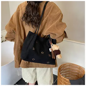 Detail of black suede tote bag with laser-cut floral patterns and a cute plush bear charm