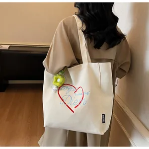 Detailansicht der cremefarbenen Canvas-Tasche mit Herzstickerei und Blumenanhänger