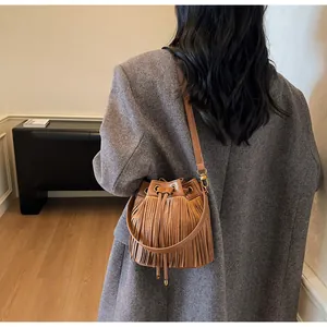 Close-up of brown suede bucket bag featuring long fringe tassels and a drawstring closure