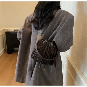Detail of a dark brown suede bucket bag featuring long fringes and drawstring closure