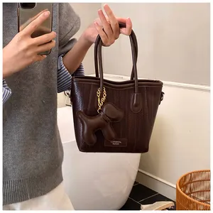 Close-up of a coffee brown woven crossbody bag featuring a cute puppy doll pendant