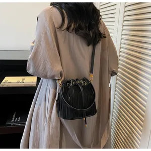 Close-up of black fringe bucket bag with gold hardware worn by a model in a studio
