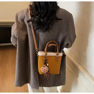 Detail of yellow suede bucket bag with white faux fur trim and furry charm accessory