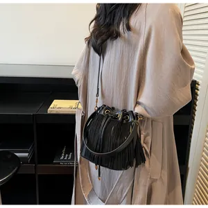 Detail of black drawstring bucket bag with decorative fringe and golden metal hardware