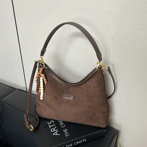 Detail of dark brown suede tote bag with leather strap and wooden bead charm accessory