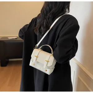 Minimalist white leather crossbody bag worn over black coat with gold metal buckle