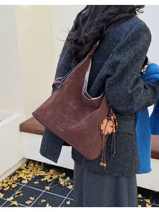 Detail of a brown suede tote bag with flower charm and logo on a park bench