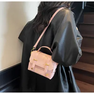 Detail of light pink square crossbody bag with gold hardware on a black leather coat