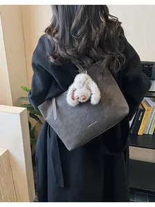 Close-up of grey tote bag with plush rabbit charm and white stitching on a black coat