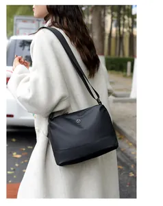 Detail of black minimalist crossbody bag with silver logo on a chic wool coat