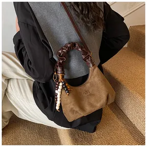 Detail of brown suede dumpling bag with quilted texture and beaded tassel charm