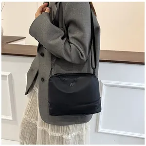 Close-up of black crossbody bag with silver logo worn by a model in modern interior