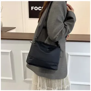 Model wearing a black nylon shoulder bag with adjustable strap in minimalist room