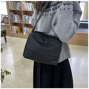 Close-up of black nylon shoulder bag with circular metal logo and stitching details