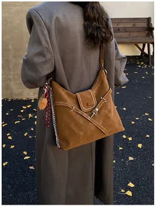 Detail of dark brown suede tote bag with metal chain and plush charm in autumn setting