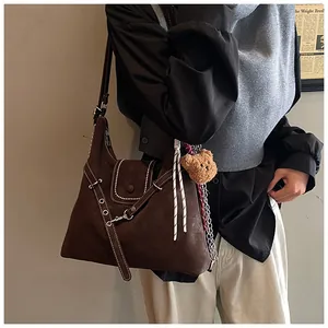 Close-up of deep brown suede shoulder bag with contrast stitching and teddy bear charm