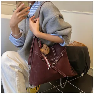 Detail of burgundy suede tote bag featuring contrast stitching and plush bear charm