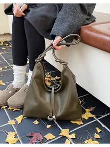 Detail of olive green hobo bag with knotted strap and ring on autumn leaves ground