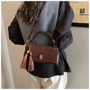 Detail of dark brown suede shoulder bag with dual tassels and gold metallic twist lock