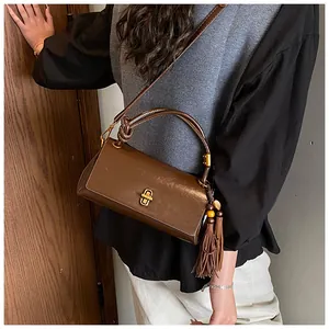 Detail view of dark brown underarm bag featuring a golden clasp and vintage tassel charm