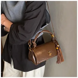 Detail of dark brown leather underarm bag featuring a gold twist lock and tassel charm