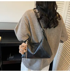 Dettaglio borsa hobo nera con cuciture diagonali e ciondolo orsetto marrone