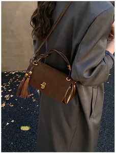 Detail of dark brown underarm bag with suede texture, gold twist lock and knot handle