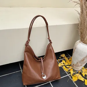 Brown leather large tote hobo bag with slender straps and silver pendant on stone steps