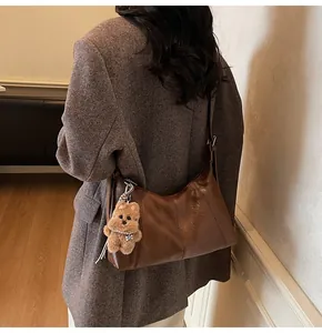 Dettaglio della borsa hobo marrone scuro con ciondolo a cucciolo su un blazer grigio